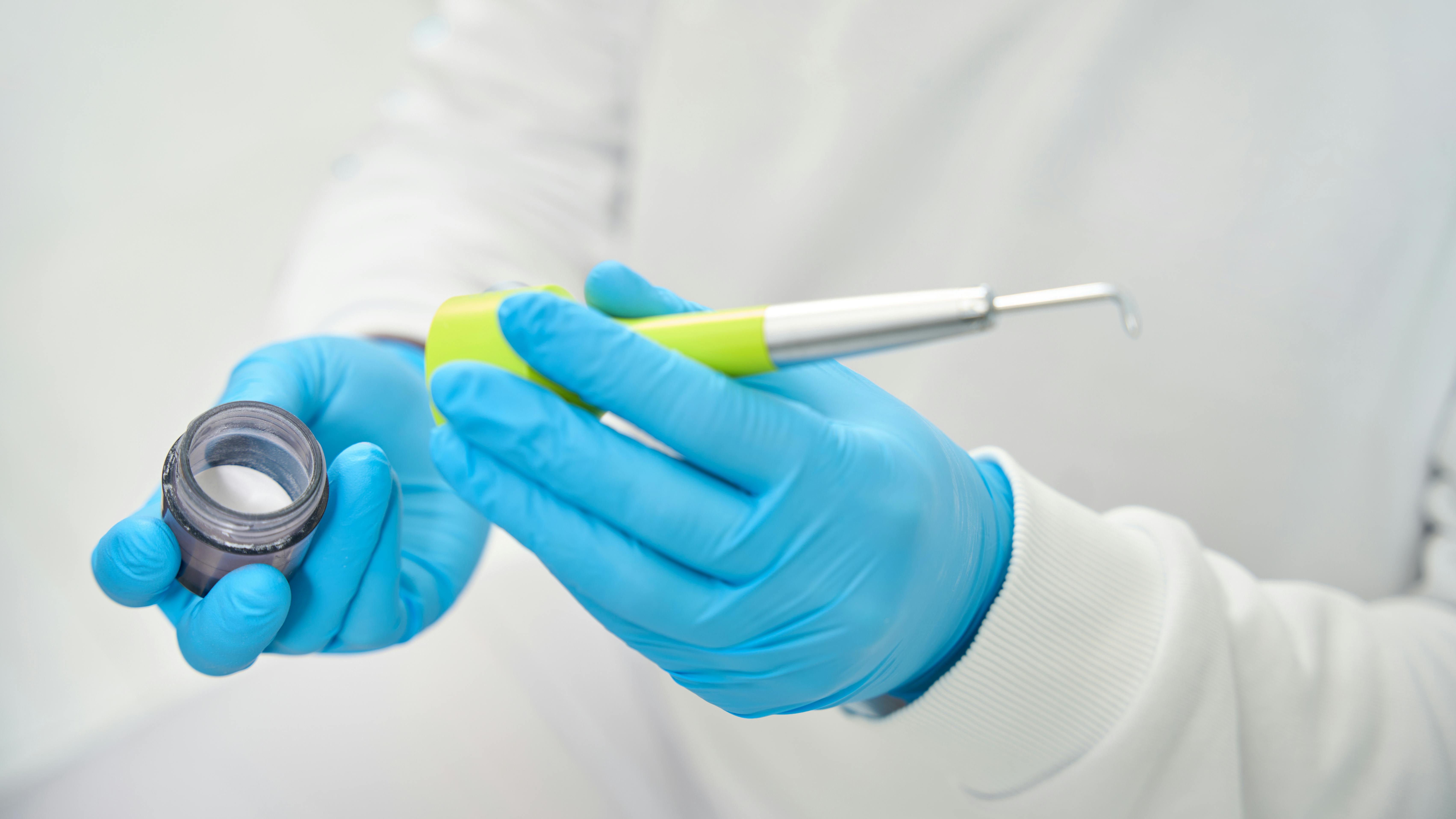 Gloved hands holding air polisher and erythritol powder