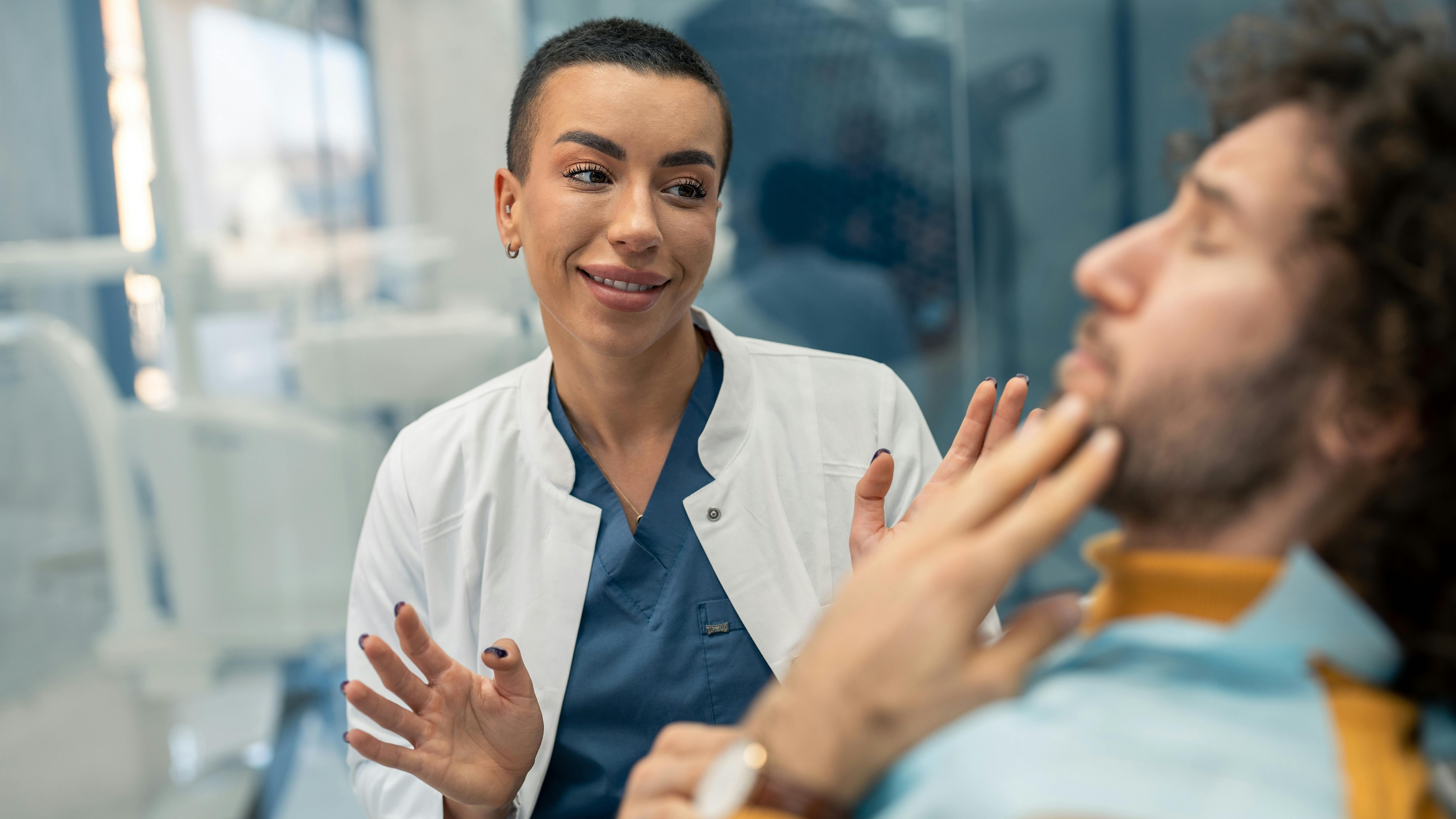 Woman in lab coat mid-conversation with male dental patient holding jaw