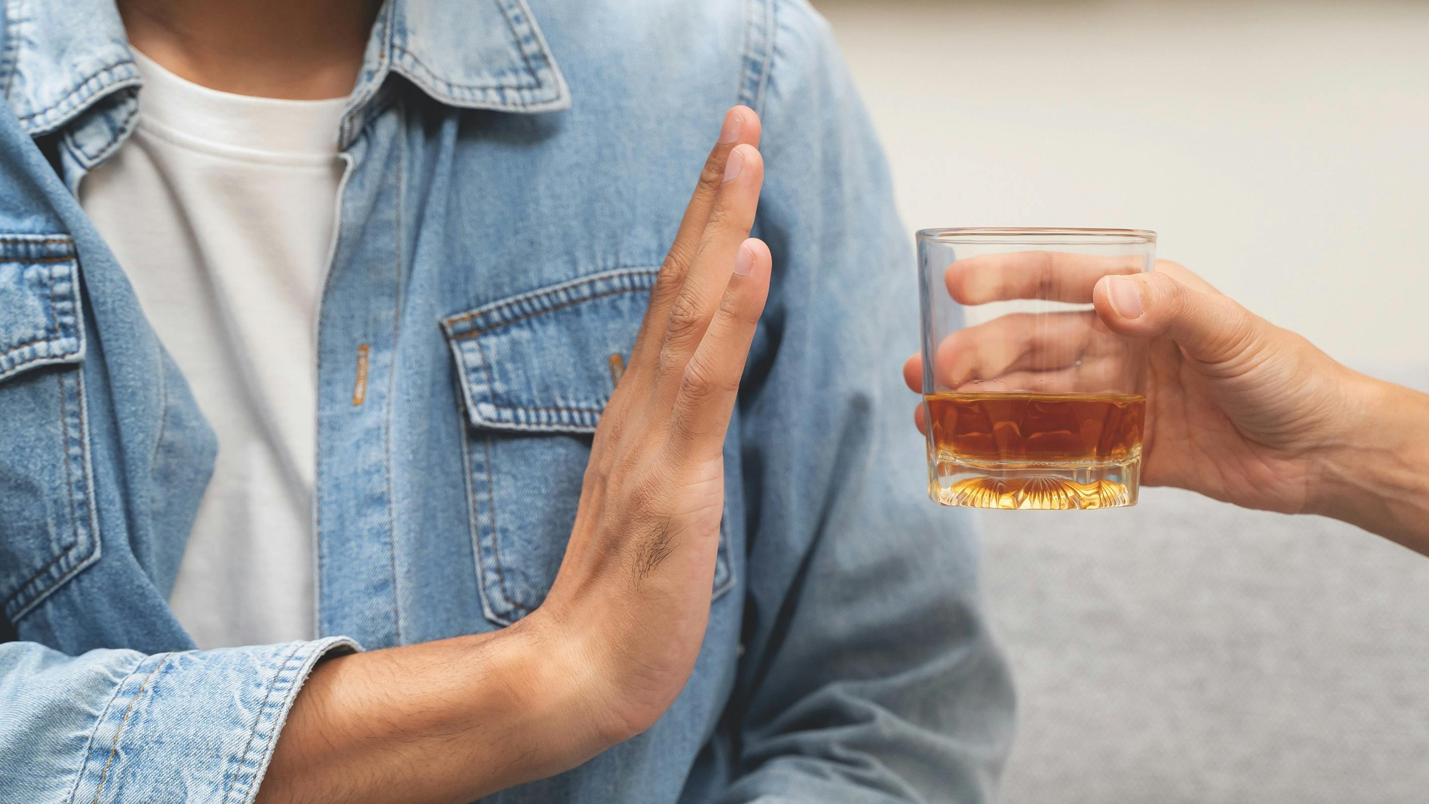 person gesturing 'no' to a glass of alcohol