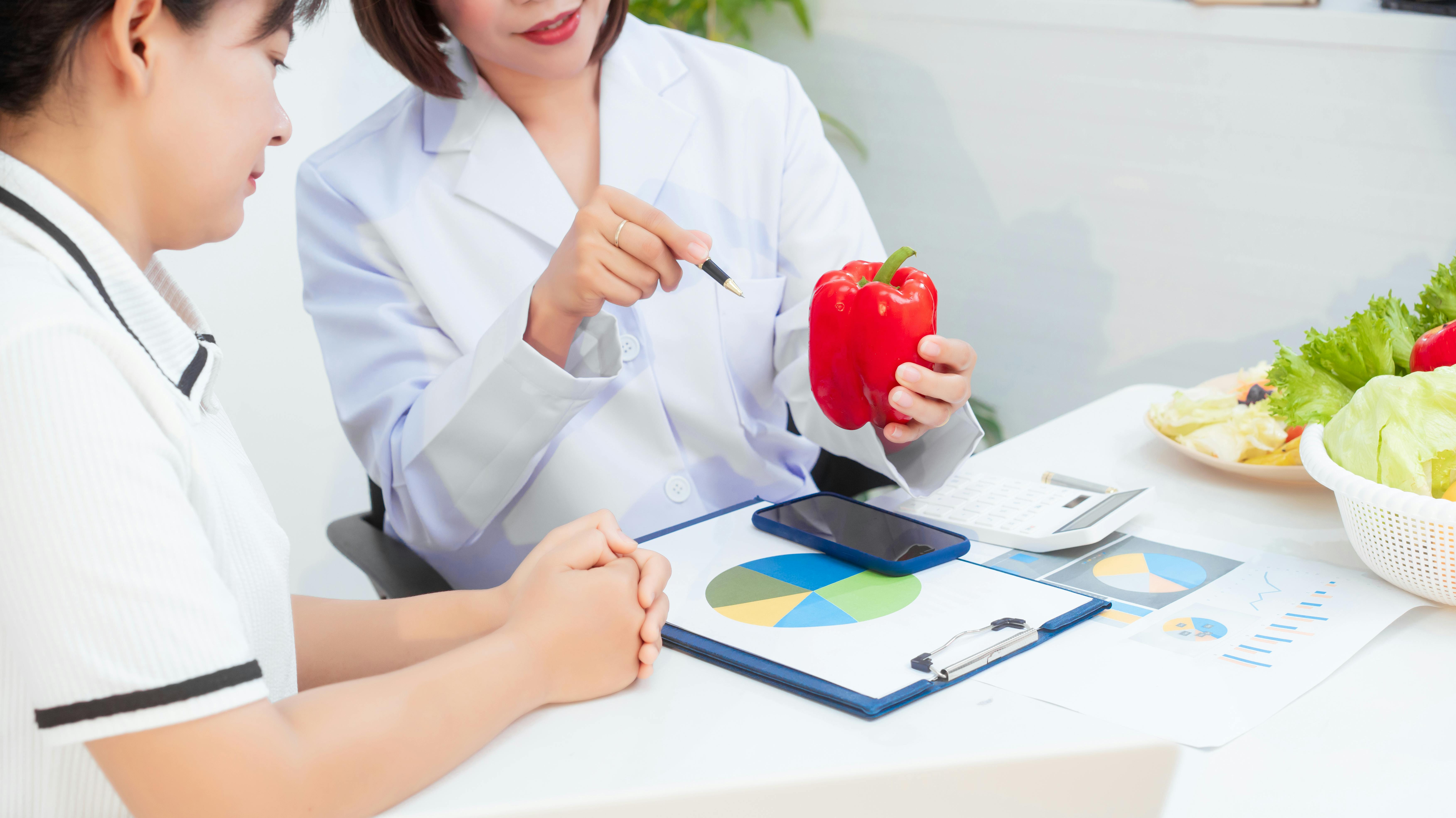 health-care professional holding a red bell pepper and talking to a patient about nutrition
