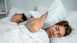 woman covering her ear with a pillow to drown out the snoring of her partner woman covering her ear with a pillow to drown out the snoring of her partner