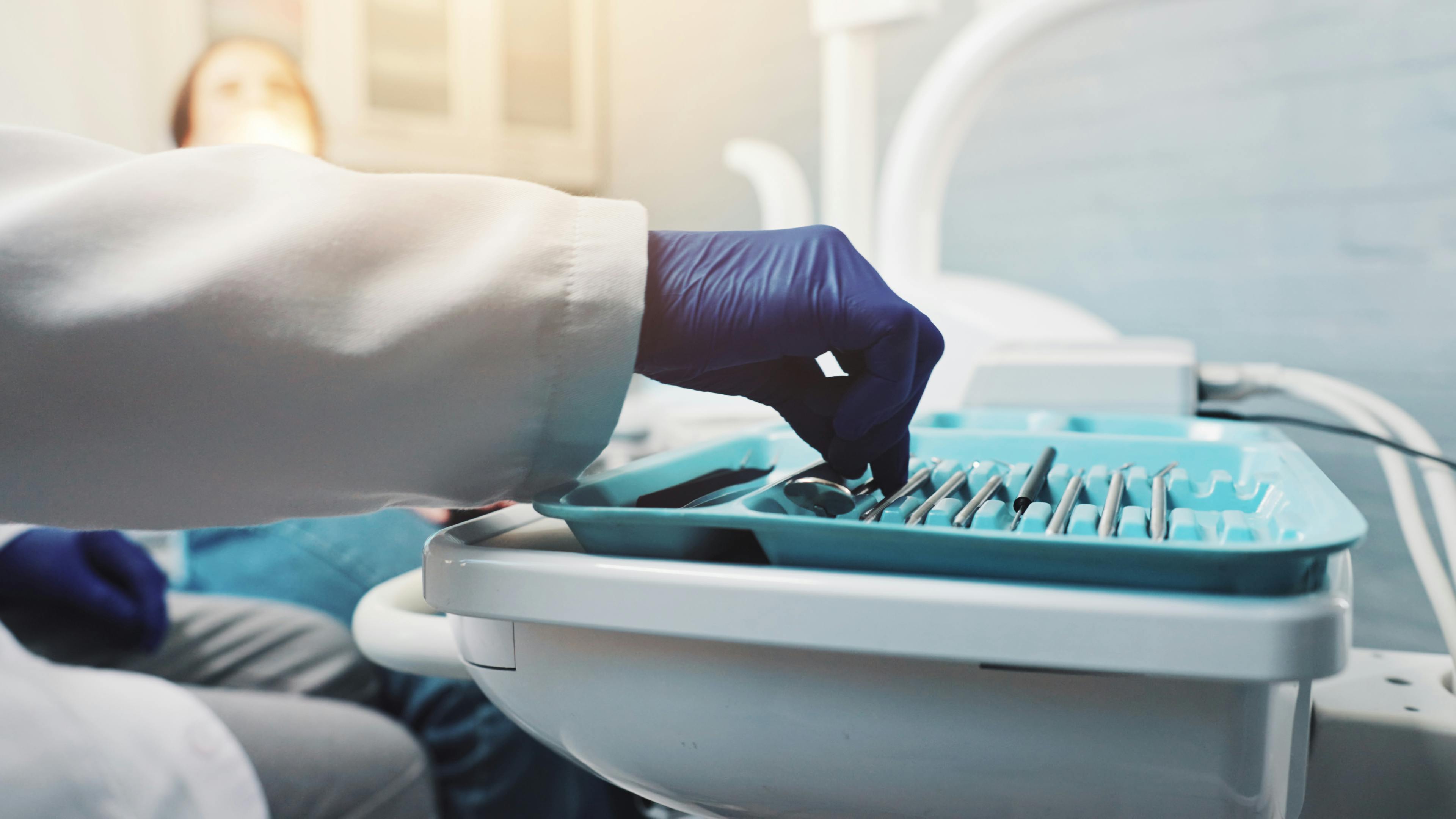 A gloved hand reaching for dental instruments