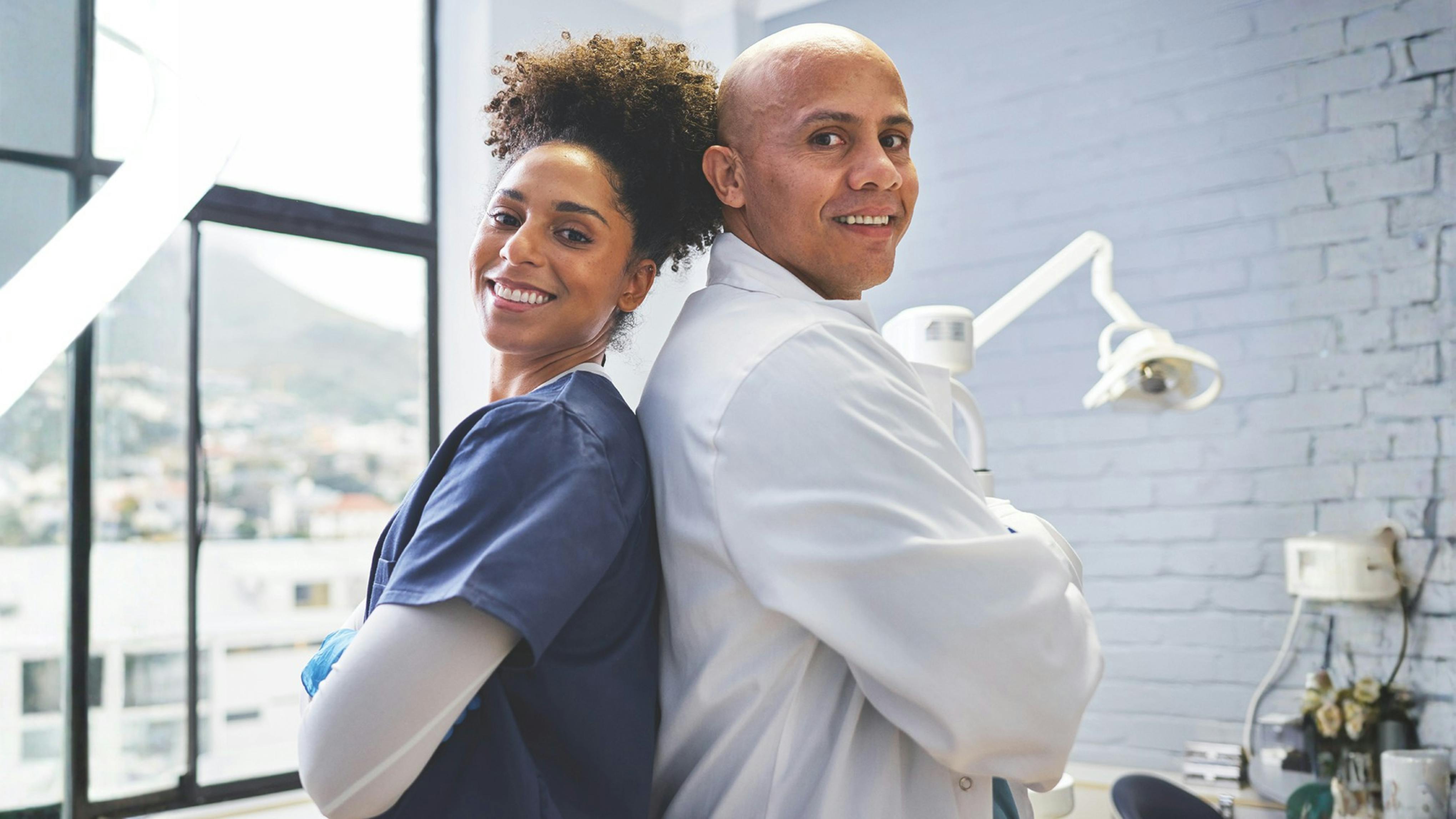 Dentist and hygienist standing back-to-back in dental operatory