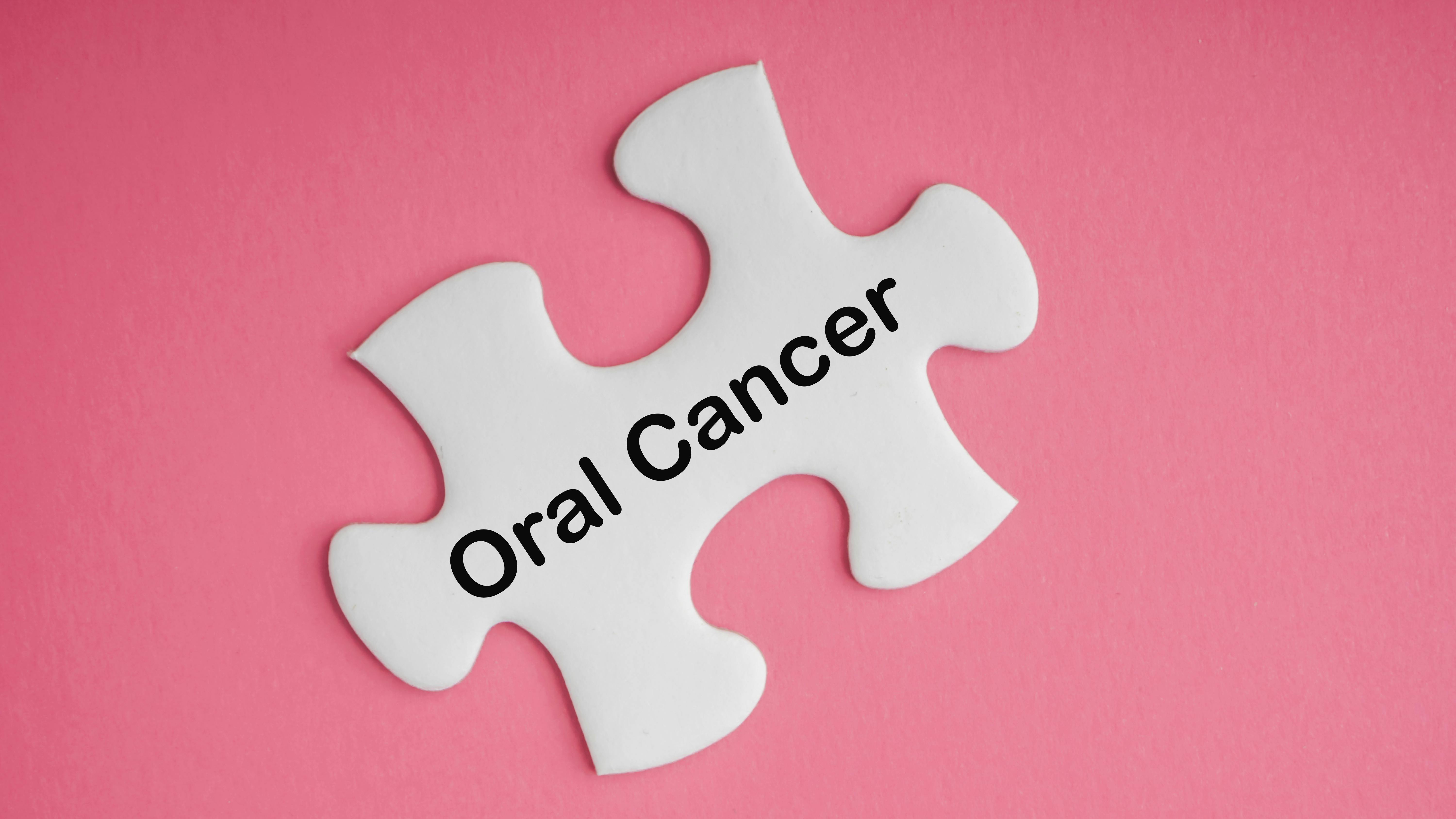a puzzle piece that says oral cancer on a pink background representing oral cancer awareness