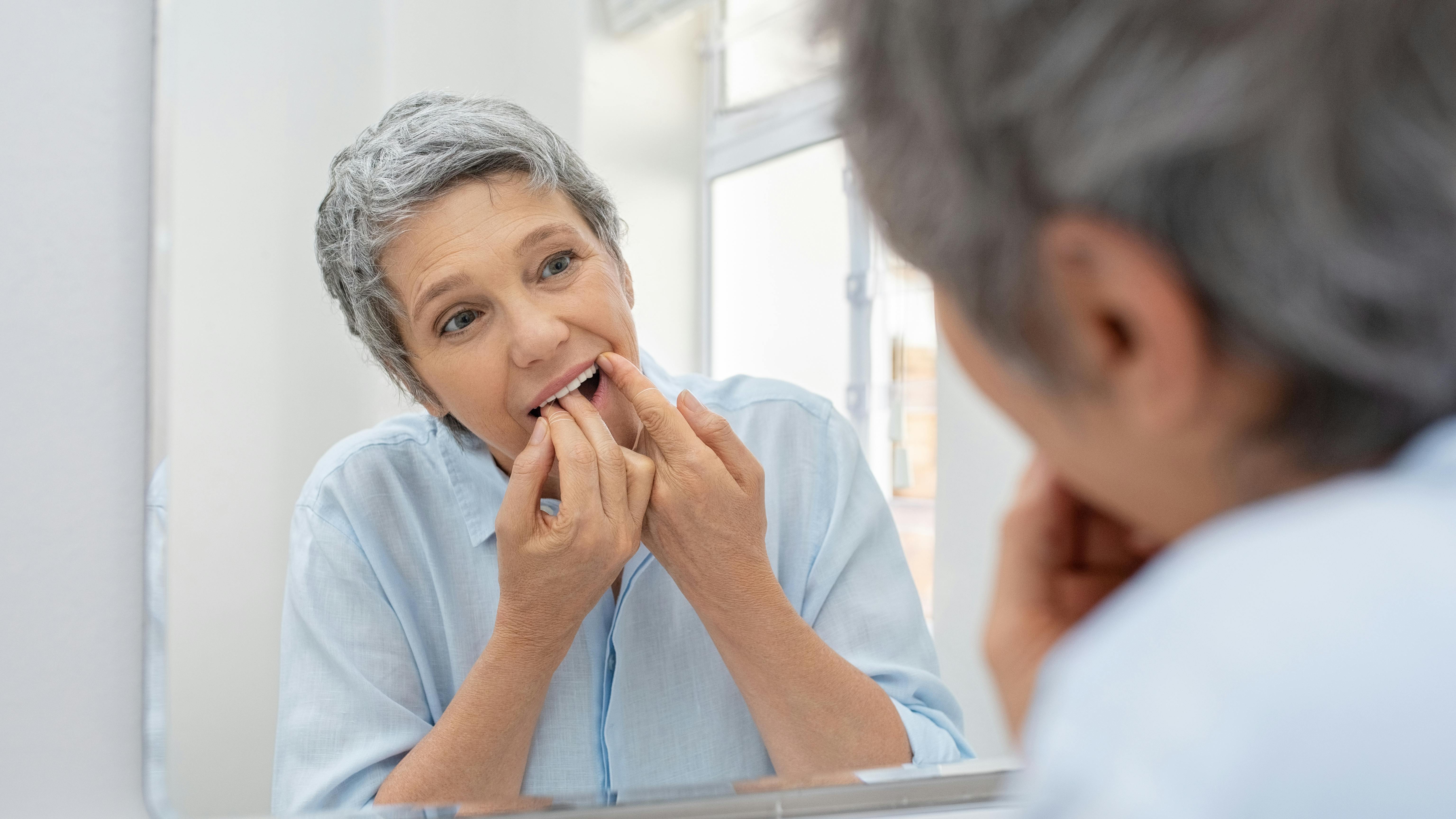 a middle-aged woman looking in the mirror and flossing her teeth