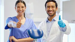 a dental hygienist and a dentist standing side by side giving a thumbs up