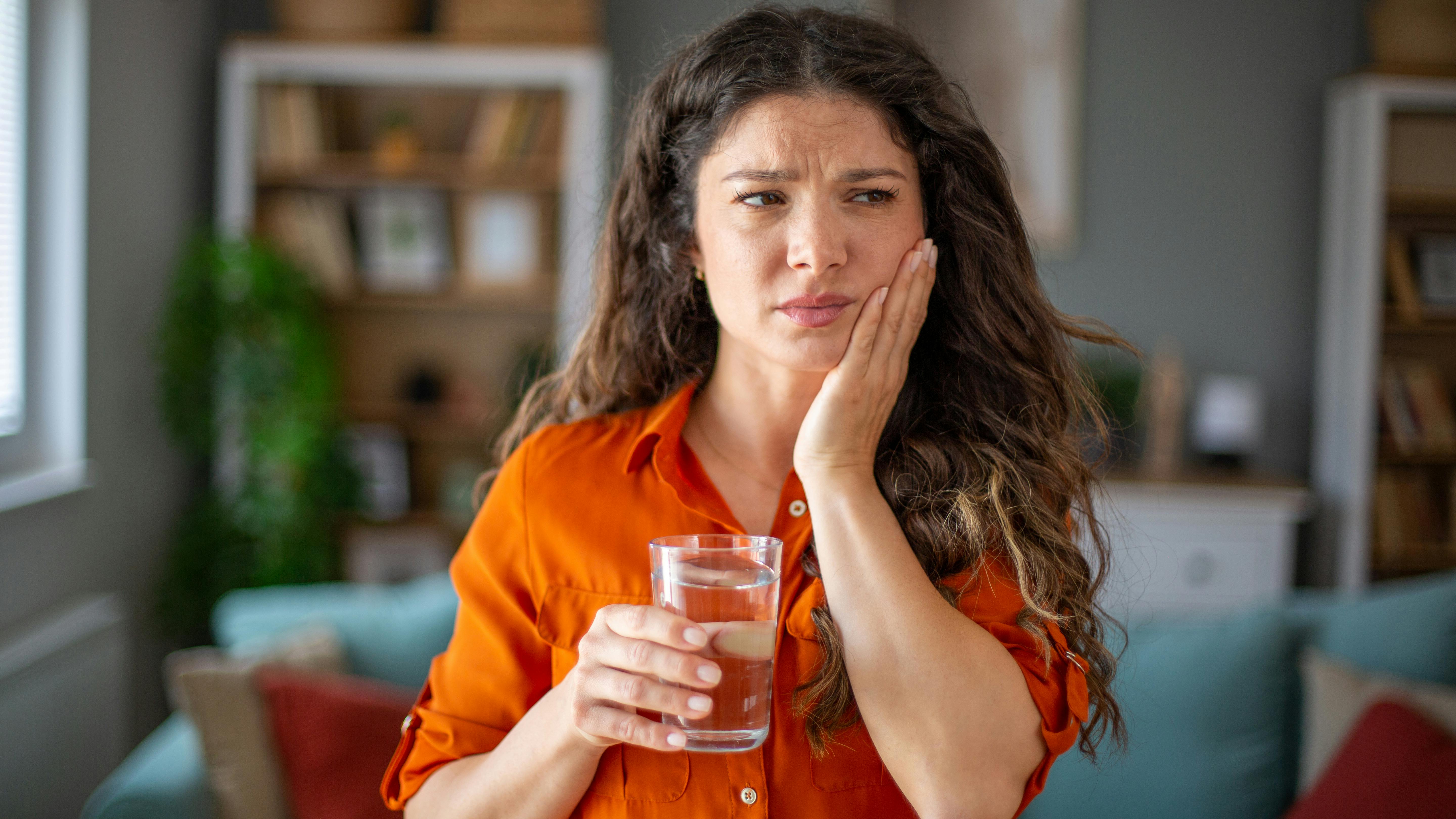 a woman holding a glass of ice water and holding the side of her face indicating tooth sensitivity