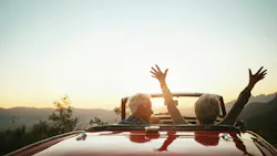 an older couple in a convertible; the woman has her hands raised high in the air in a sign of celebration of retirement an older couple in a convertible; the woman has her hands raised high in the air in a sign of celebration of retirement