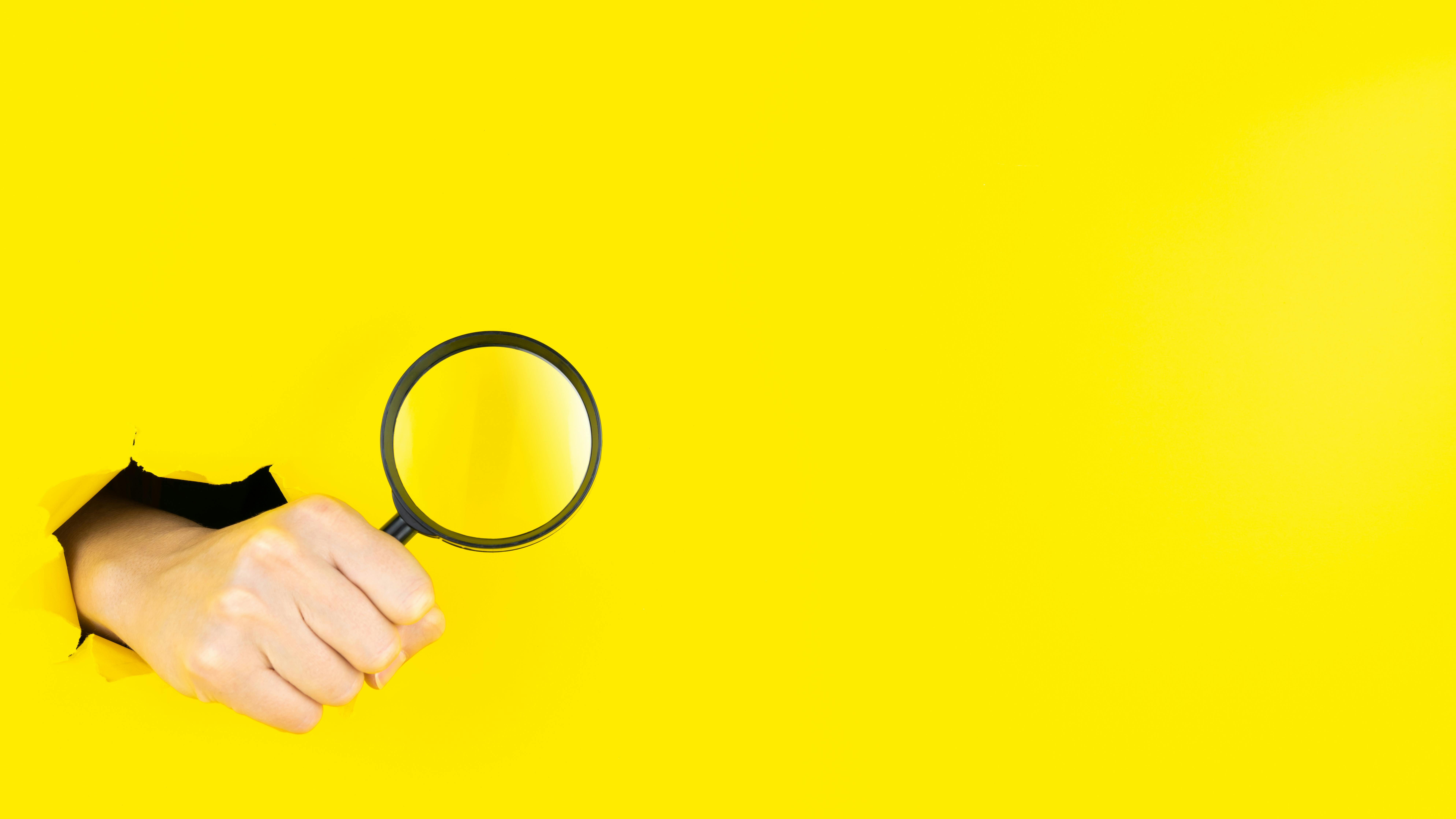 a hand bursting through the background holding a magnifying glass