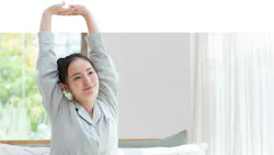 Woman sitting up in bed, stretching arms skyward