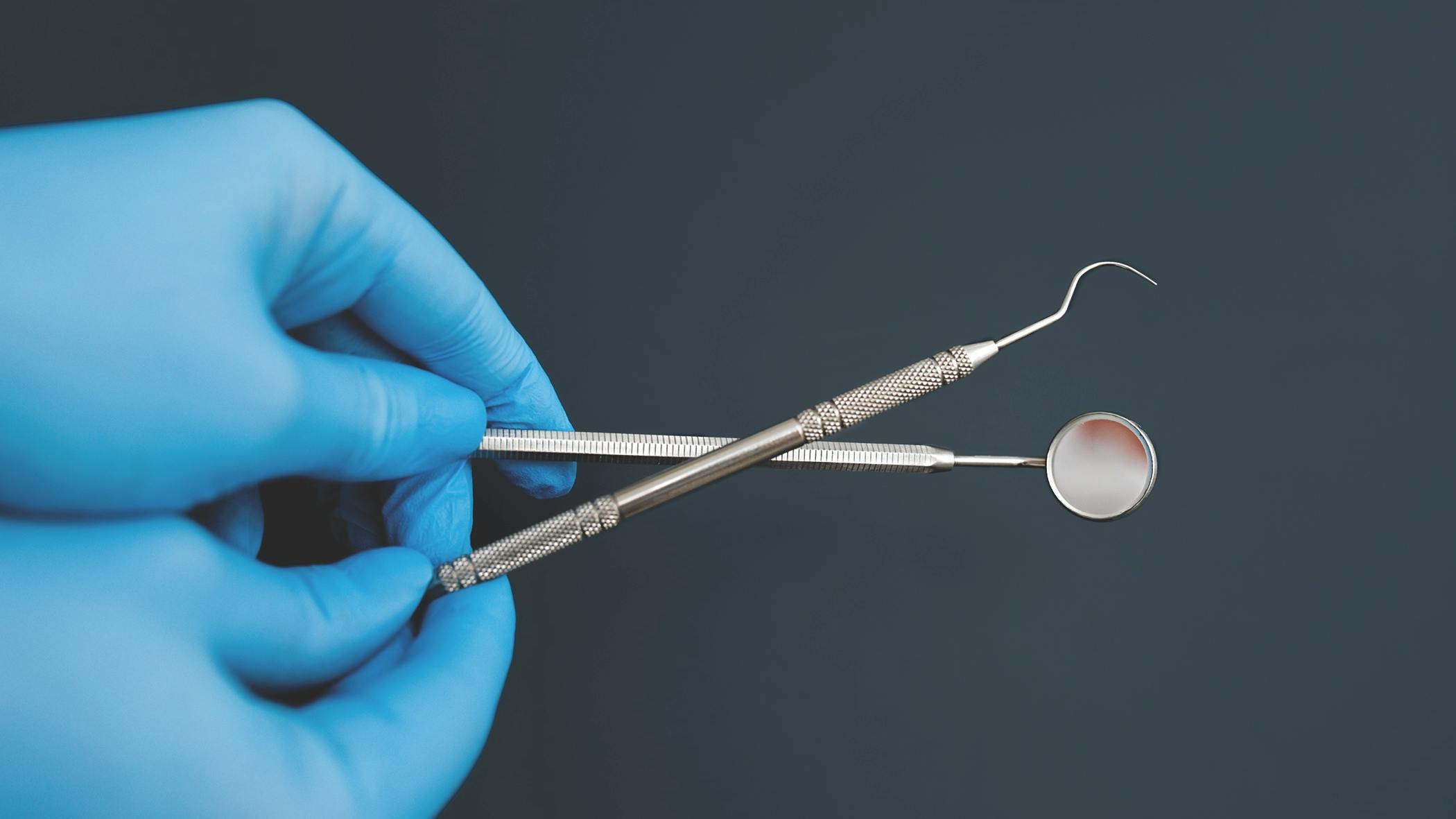 a gloved hand holding two dental hygiene instruments