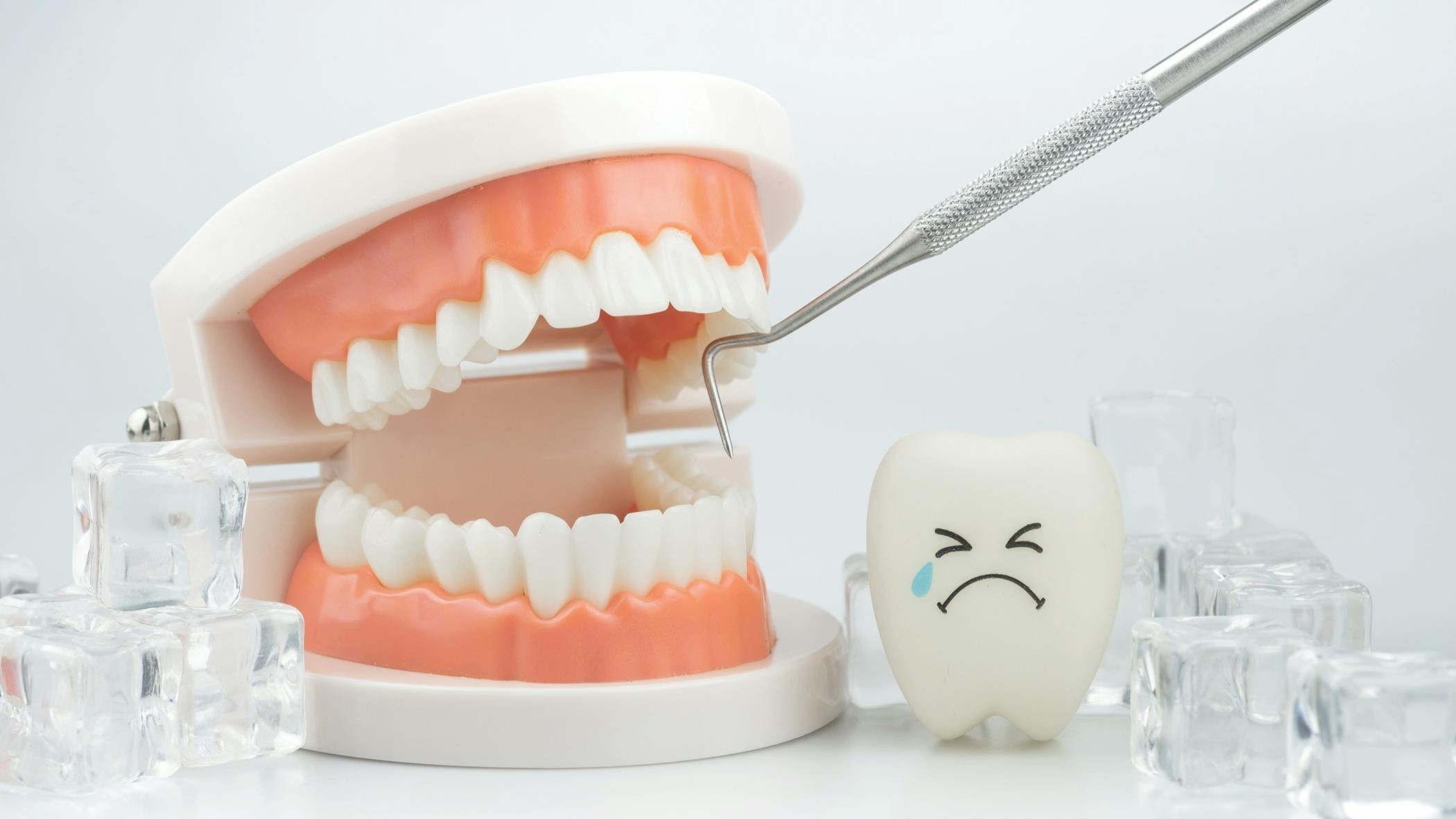 Illustration of tooth sensitivity showing a dental model, dental scaler, ice cubes, and a crying tooth icon to represent cold sensitivity and dental pain.