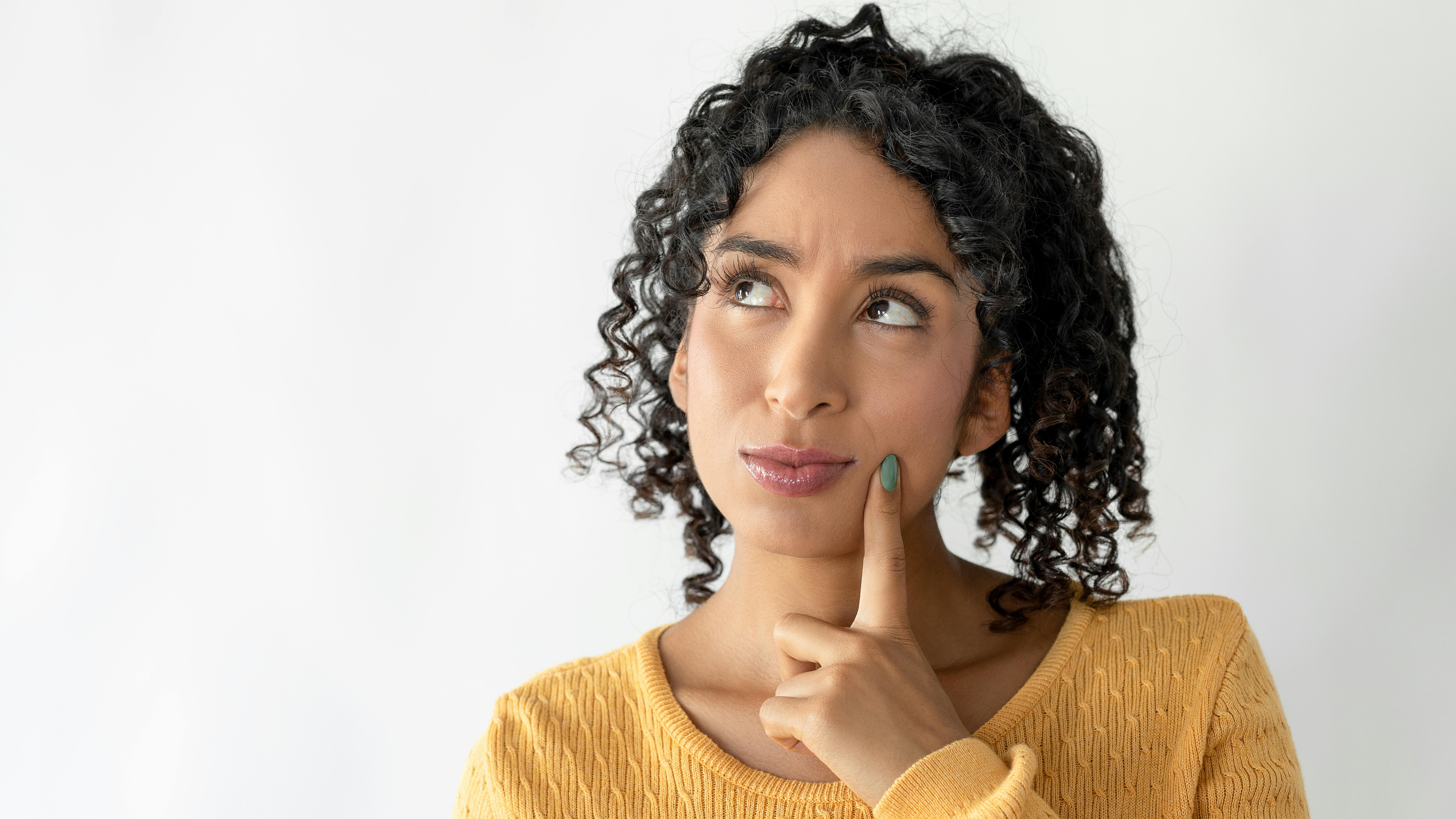 woman looking upward with one finger on the side of her face, thinking