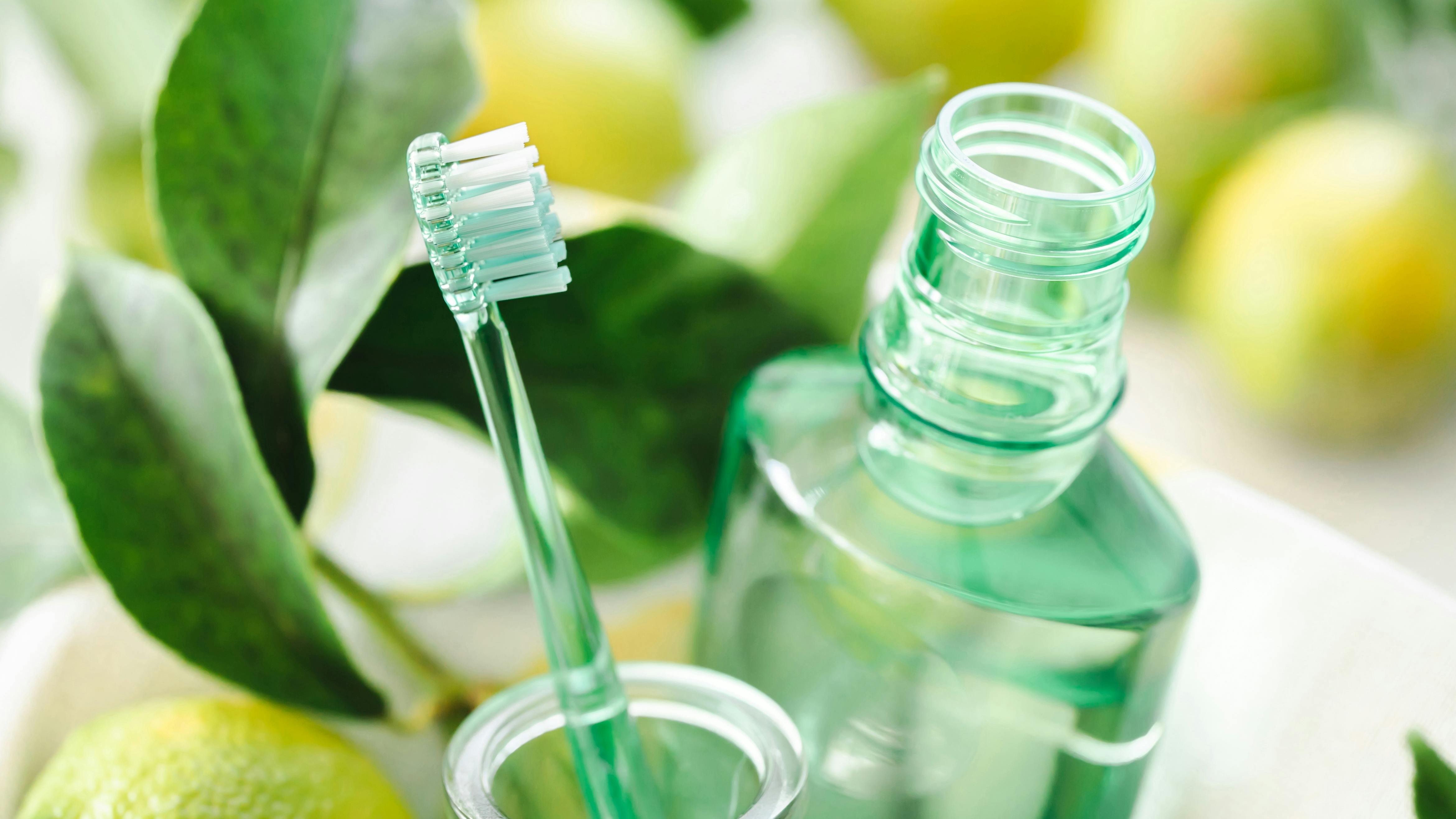 a toothbrush and mouthwash against a backdrop of leaves