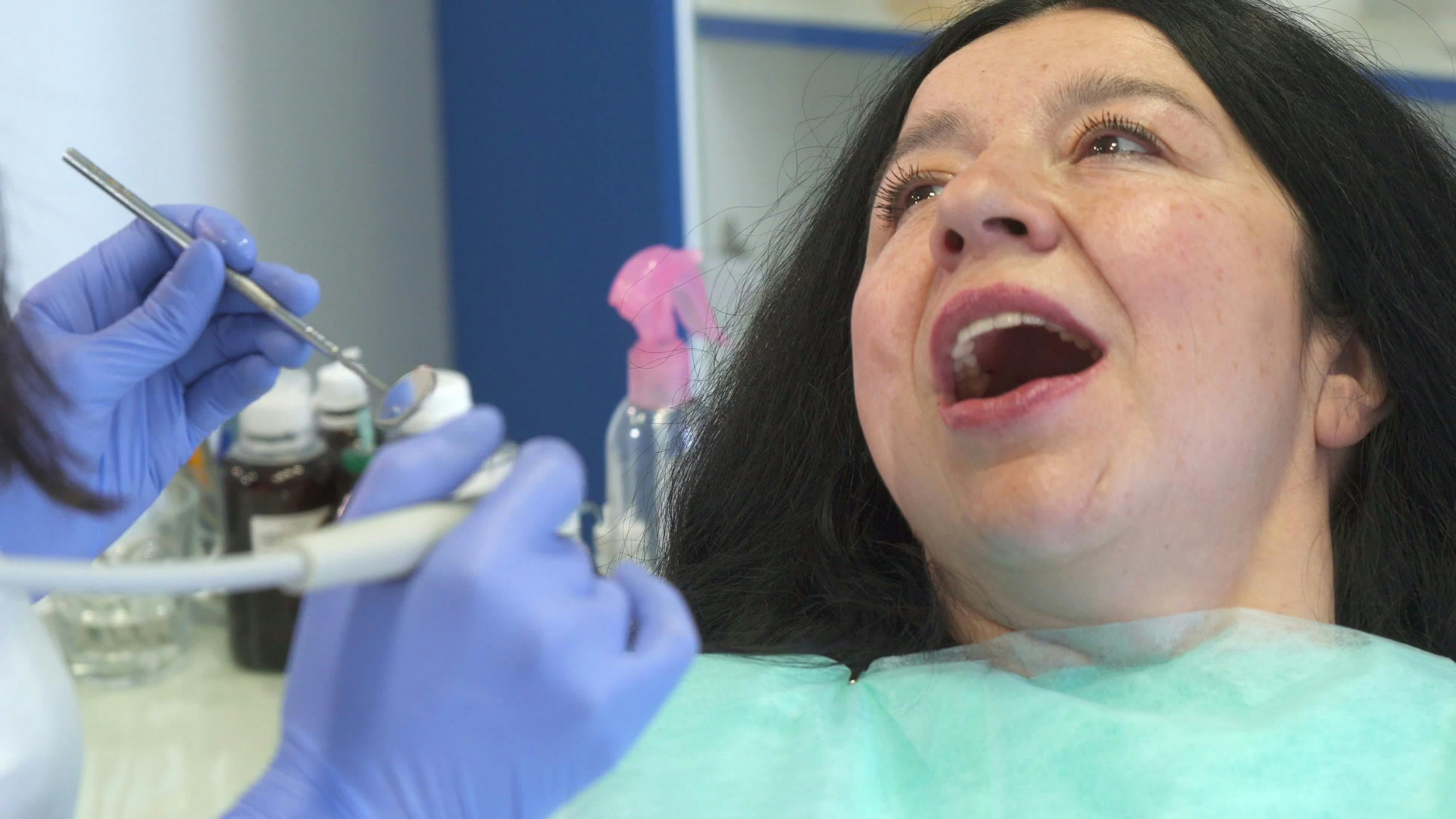 female dental patient with mouth partly open near a gloved hygienist's hands