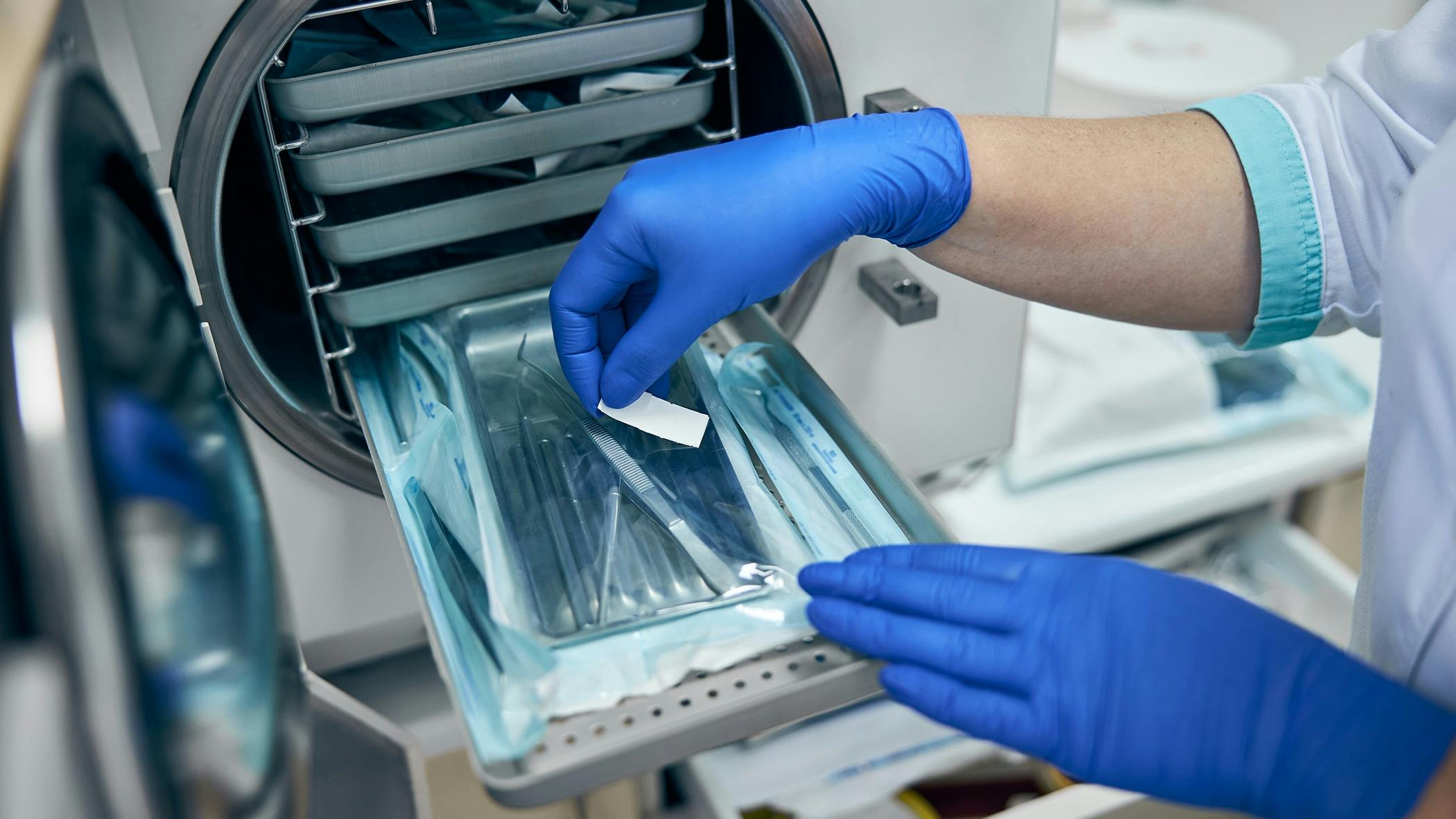 a dental professional's gloved hands working with the instruments in the sterilizer